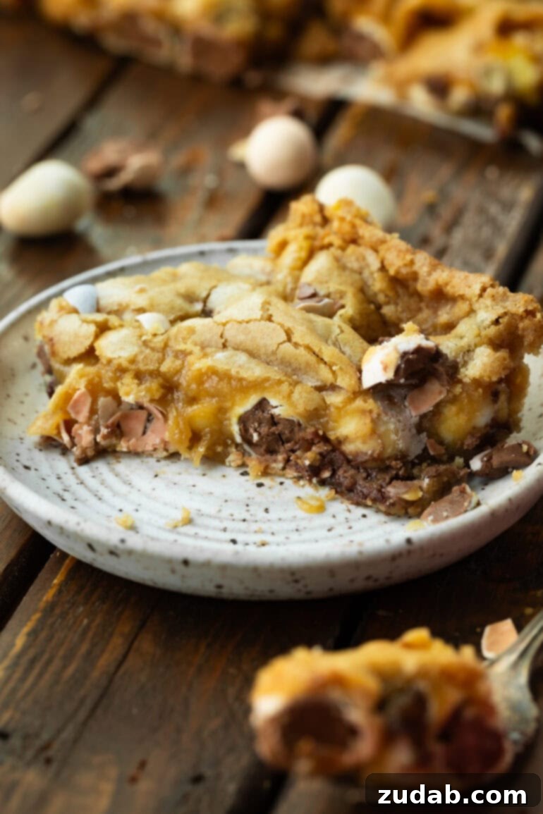 Ultimate Easter Cadbury Mini Egg Blondies 4 Two blondie squares stacked on a white plate, showing gooey chocolate and colorful Cadbury Mini Eggs.