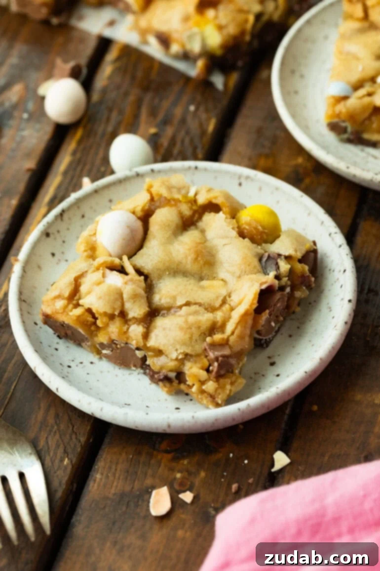 Ultimate Easter Cadbury Mini Egg Blondies 7 A slice of chewy Cadbury Mini Egg Blondie on a white spotted plate with pastel chocolate eggs on top.