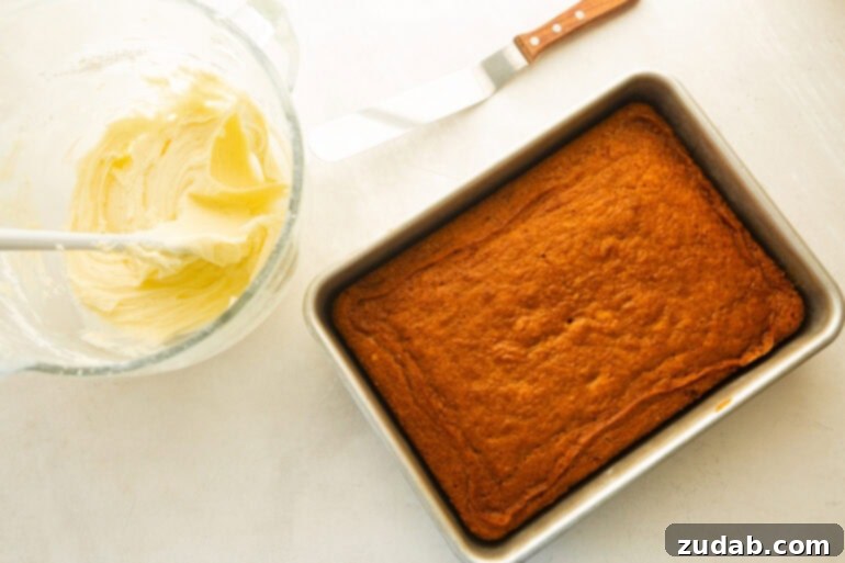 Effortless Carrot Cake: The Baby Food Secret 6 a baked 9x13 carrot cake with a bowl of cream cheese frosting in a glass bowl with an offset spatula sitting next to the bowl