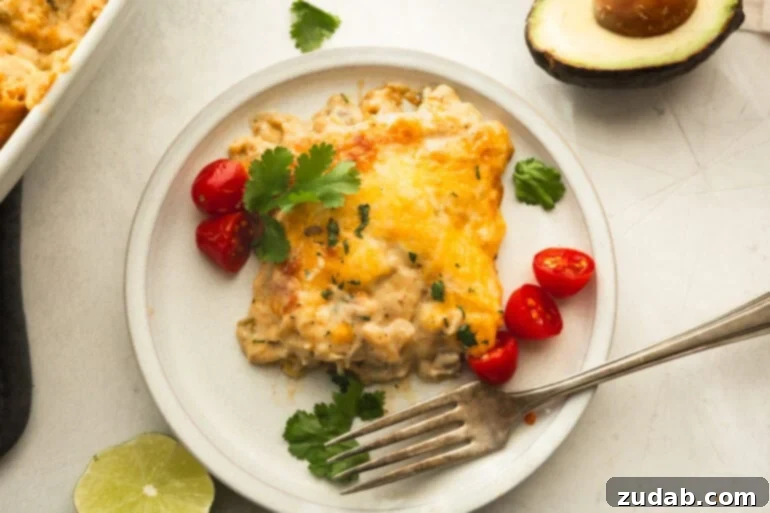 Mama's Velvety Chicken Enchilada Bake 3 a serving of creamy chicken enchilada casserole on a dinner plate with a fork sitting next to it and some halved cherry tomatoes scatted around it