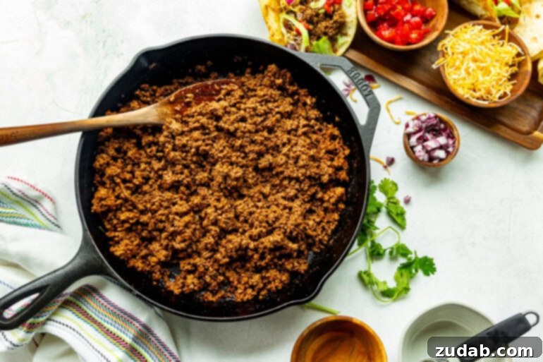 Speedy Weeknight Beef Tacos 6 a large cast iron skillet full of cooked seasoned ground beef with a wooden spoon stirring it
