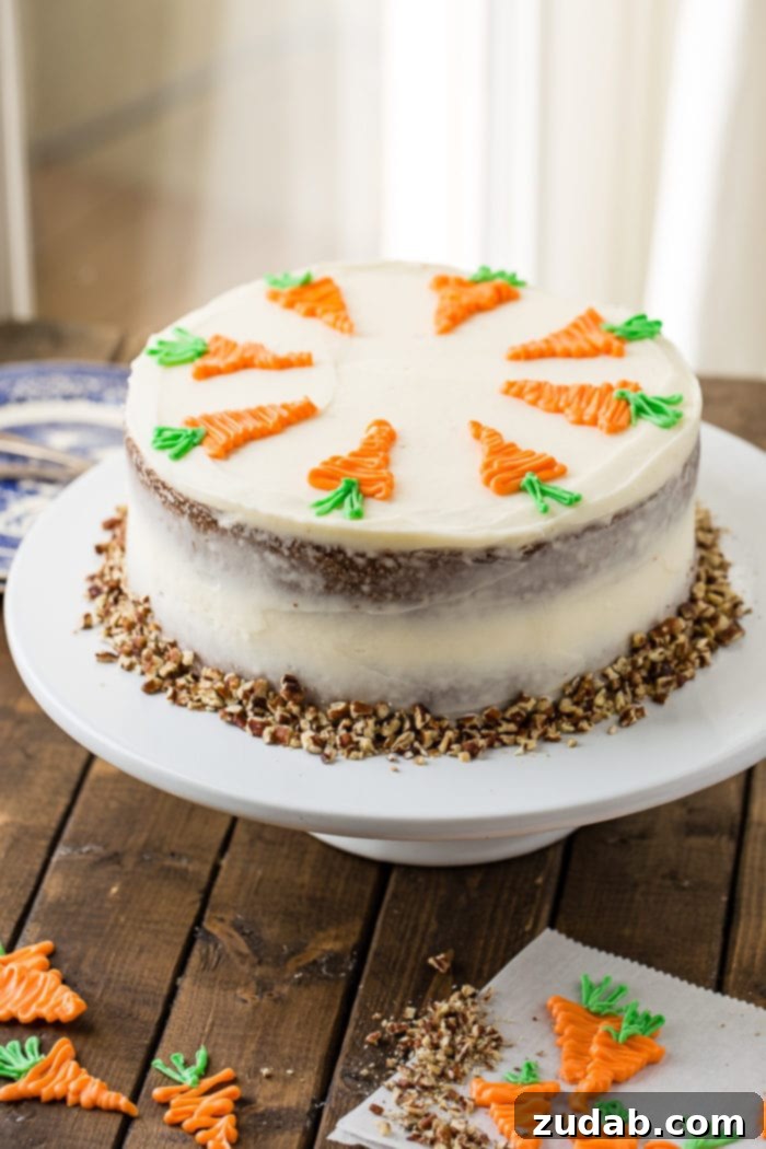 Ultimate Moist Carrot Cake with Cream Cheese Frosting 3 A two-layer carrot cake on a white cake stand, generously covered in white cream cheese frosting and adorned with white chocolate decorative carrots, surrounded by chopped walnuts at its base.