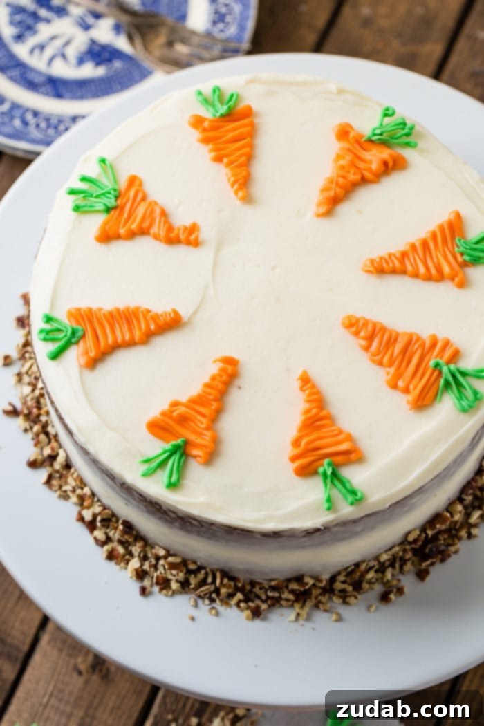 Ultimate Moist Carrot Cake with Cream Cheese Frosting 8 A carrot cake viewed from directly above, placed on a white cake plate. It is adorned with white cream cheese frosting and white chocolate decorative carrots, surrounded by chopped walnuts at its base.