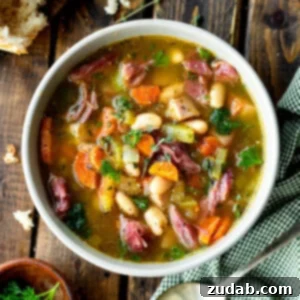 a photo of a large bowl of ham and bean soup with a large chunk of crusty bread next to it and a spoon