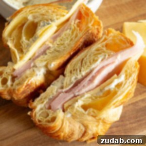 a ham and cheese sandwich on a flaky croissant that has been sliced in half so you can see the inside of each half