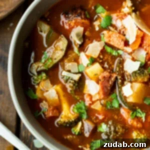 a photo of a bowl of hearty ham and vegetable soup loaded with potatoes, carrots, tomatoes, mushrooms and topped with chopped parsley