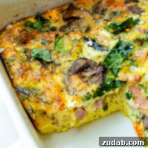 a baking dish of a baked egg, spinach and sauteed mushroom casserole with a serving missing so you can see the cross-section of the casserole