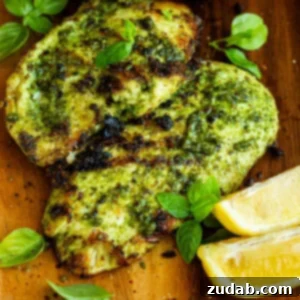 Two grilled chicken breasts coated in basil, with lemon wedges on a cutting board.