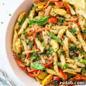 A large bowl full of penne pasta tossed with fresh vegetables and a creamy sauce.