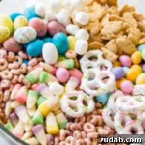Easter snack mix in a clear glass bowl with berry Cheerios, Easter candy corns, yogurt covered pretzels, Robin eggs, Easter M&Ms. mini marshmallows and bunny cookies.