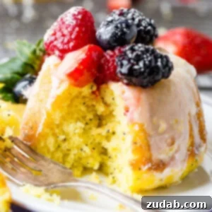 A photo of a mini lemon poppy seed bundt cake on on a silver wire cooling rack with a lemon glaze on top and fresh berries.