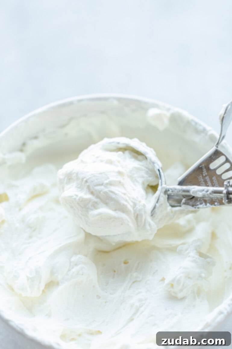 Luxurious Mascarpone Whipped Cream 4 A close-up photo depicting someone skillfully using an ice cream scoop to gather a generous portion of thick, fluffy, and perfectly set mascarpone whipped cream from a large mixing bowl.