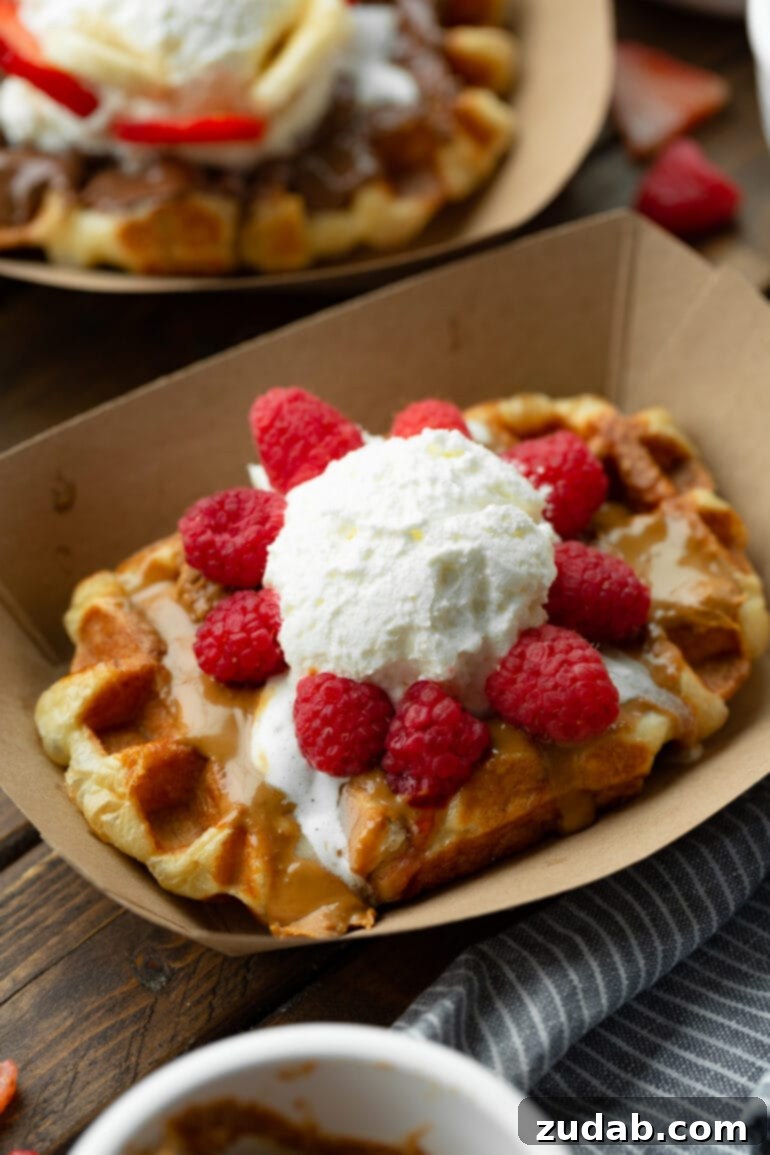 Luxurious Mascarpone Whipped Cream 5 A large, golden rectangular waffle, exquisitely topped with a luscious swirl of Biscoff cookie butter, a generous cloud of mascarpone whipped cream, and vibrant fresh raspberries, creating a truly indulgent and visually appealing dessert.