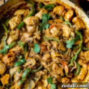 A skillet full of golden chicken chunks, sautéed bell pepper slices, onion slices, and sliced mushrooms in a creamy sauce.