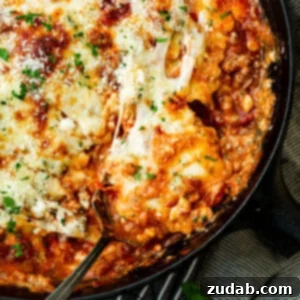 A serving of skillet lasagna being scooped out of a cast iron skillet.