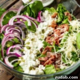 A photo of a large glass bowl full of a fresh spinach salad topped with thinly sliced red onions, cottage cheese, crispy bacon bits and shredded swiss cheese.