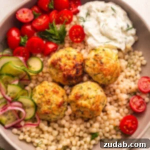A plate of pearl cous cous topped with chicken meatballs with a side of cherry tomatoes and tzatziki