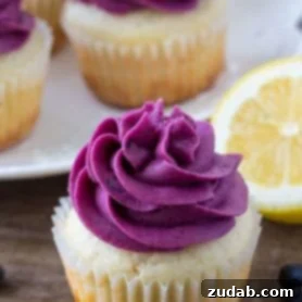 Moist lemon cupcake topped with blueberry frosting with a a plate of lemon blueberry cupcakes in the background.