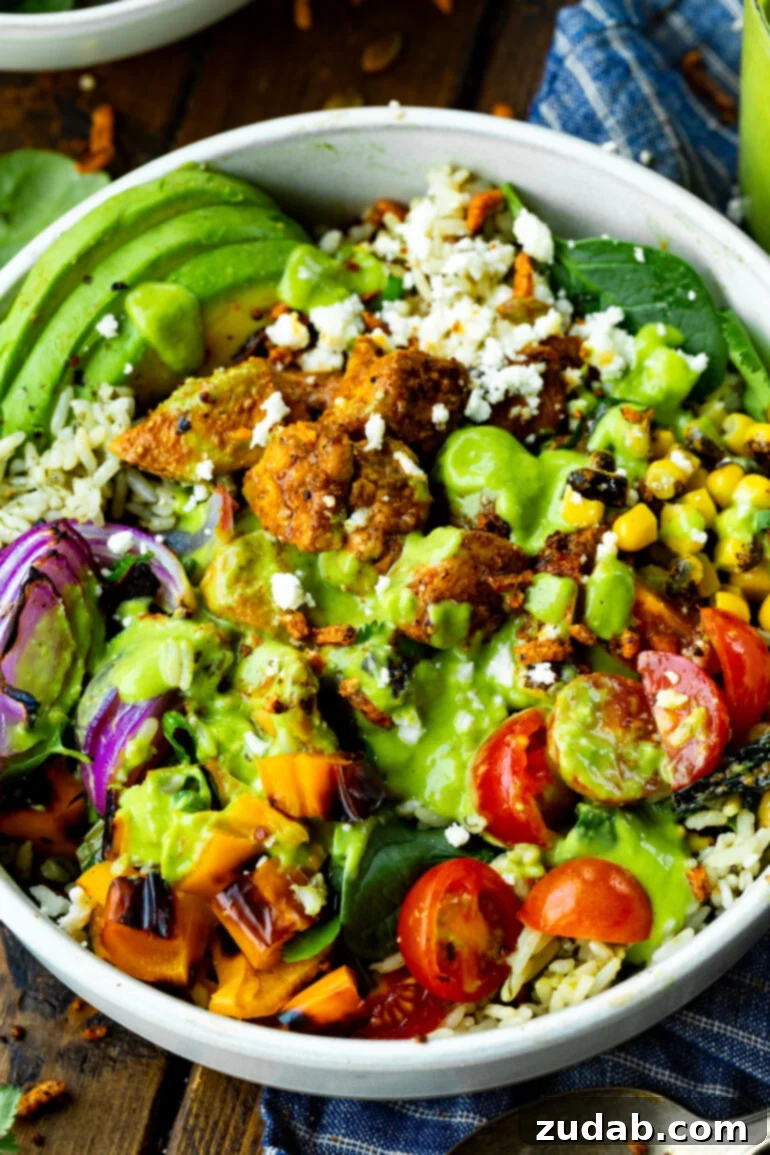 Easy Authentic Cinco de Mayo Recipes for Your Fiesta 18 a photo of a mexican chicken burrito rice bowl topped with half cherry tomatoes, corn, red onion, crumbled queso fresco, seasoned chunks of chicken and a creamy avocado dressing.