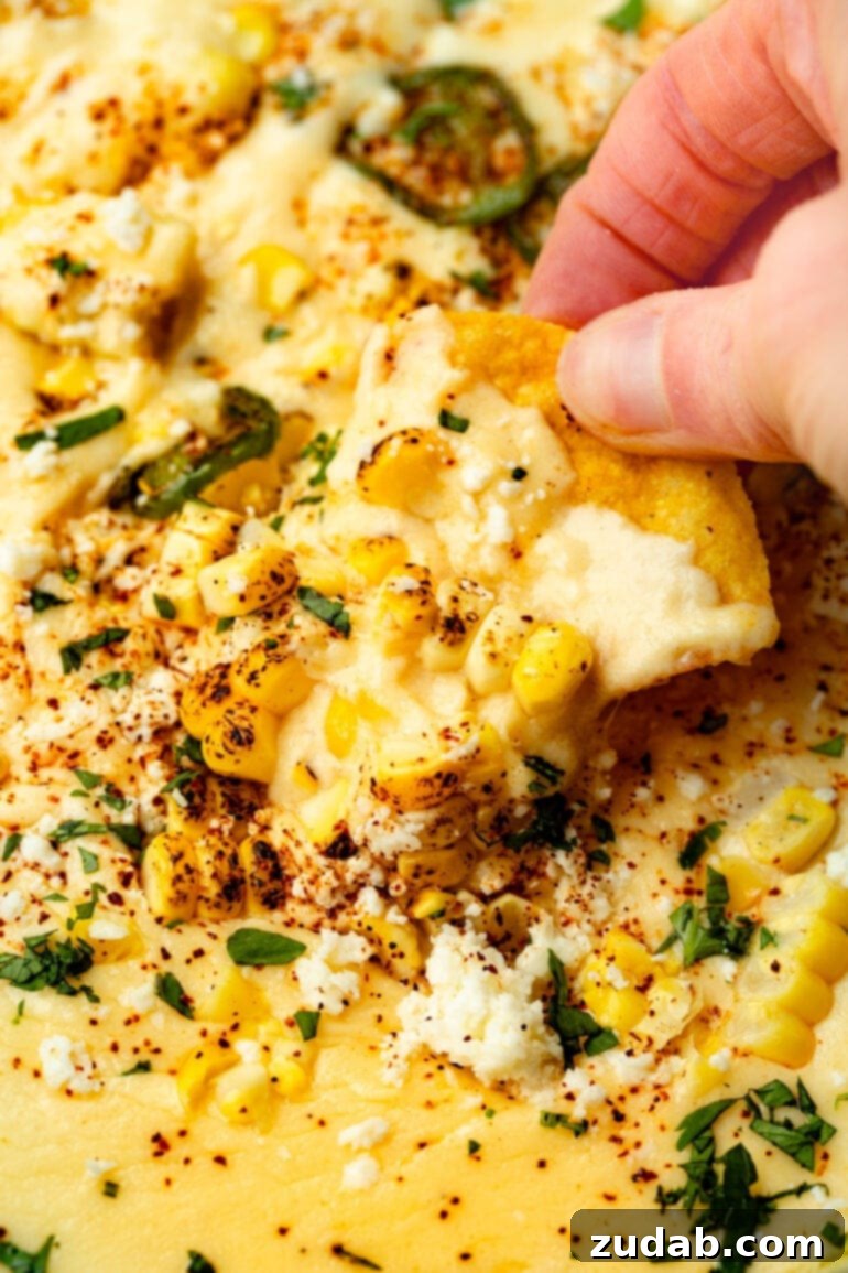 Easy Authentic Cinco de Mayo Recipes for Your Fiesta 38 someone lifting a corn tortilla chip from a skillet of elote queso dip