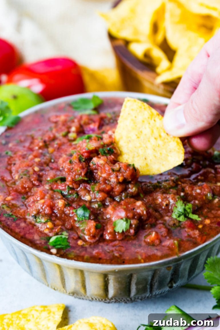 Easy Authentic Cinco de Mayo Recipes for Your Fiesta 40 A bowl of homemade salsa in which a tortilla chip is being dipped. The salsa is sprinkled with cilantro leaves and has cilantro and roma tomatoes and a lime in the background. There is also a wooden bowl of chips in the background.