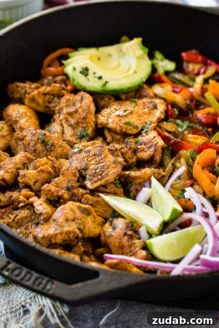 Easy Authentic Cinco de Mayo Recipes for Your Fiesta 10 A photo of a cast iron skillet full of chicken fajita filling - cooked chicken, sauteed peppers and onions, lime wedges, sliced purple onion, and sliced avocados.