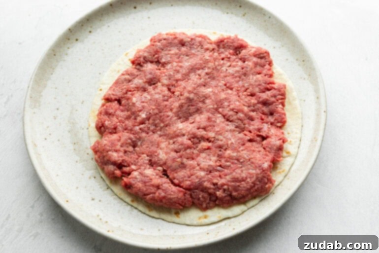 Smash Burger Taco Sensation 4 A flour tortilla topped with a thin layer of seasoned ground beef, ready to be smashed and cooked.