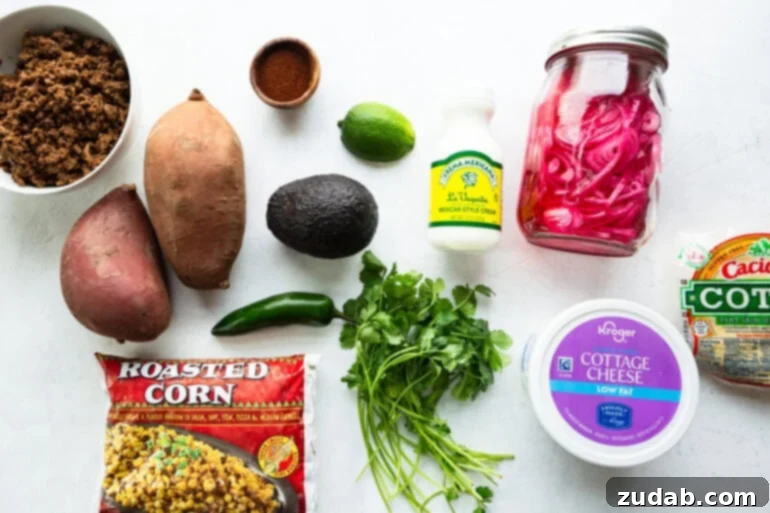 Street Corn Ground Beef Sweet Potato Power Bowl 3 All the fresh ingredients laid out for a street corn ground beef sweet potato bowl, including vibrant sweet potatoes, creamy Mexican crema, zesty lime, ripe avocado, spicy jalapeño, fresh cilantro, tangy pickled red onions, and sweet corn.