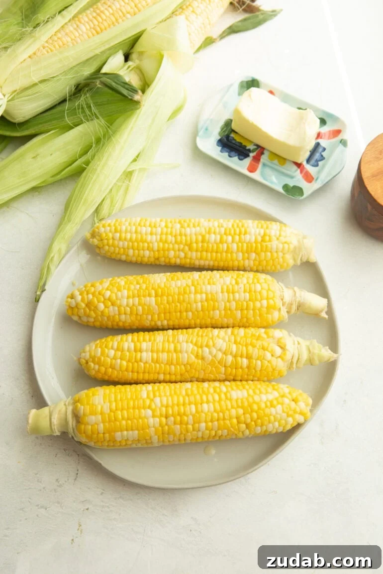 How to Cook Corn on the Cob Perfectly Every Time 5 four ears of corn on a plate with a stick of butter next to the plate