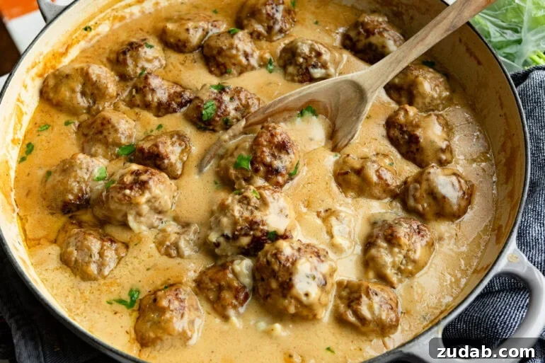 Classic Swedish Meatballs with Creamy Gravy 7 swedish meatballs sitting in thick gravy sauce being stirred with a wooden spoon