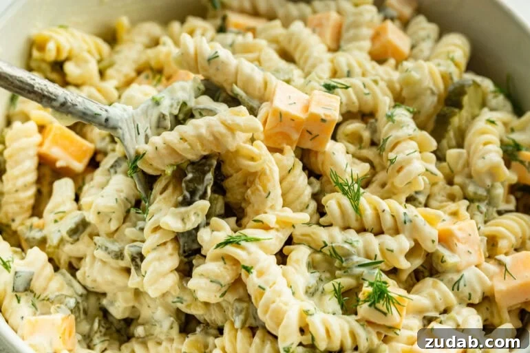 Creamy Dill Pickle Pasta Salad with Crunchy Cucumbers 3 A close up of dill pickle pasta salad with pasta in a creamy sauce, pickles, cheddar cheese, and garnished with dill.