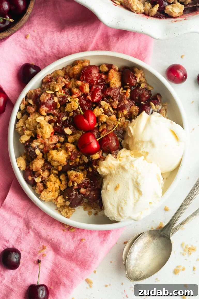 Classic Old-Fashioned Cherry Crisp with Oat Topping 2 a serving of cherry crisp with oatmeal topping and two scoop of vanilla ice cream on the side