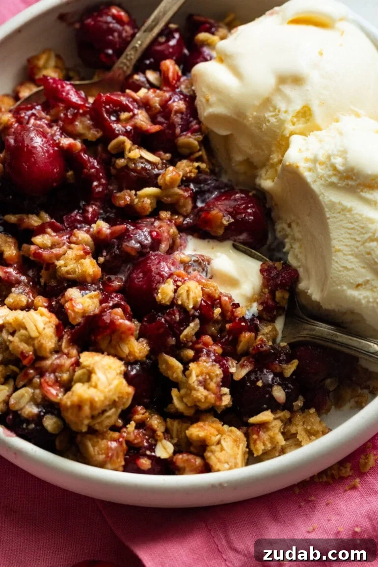 Classic Old-Fashioned Cherry Crisp with Oat Topping 3 someone scooping up a bit of cherry crisp with vanilla ice cream on the side