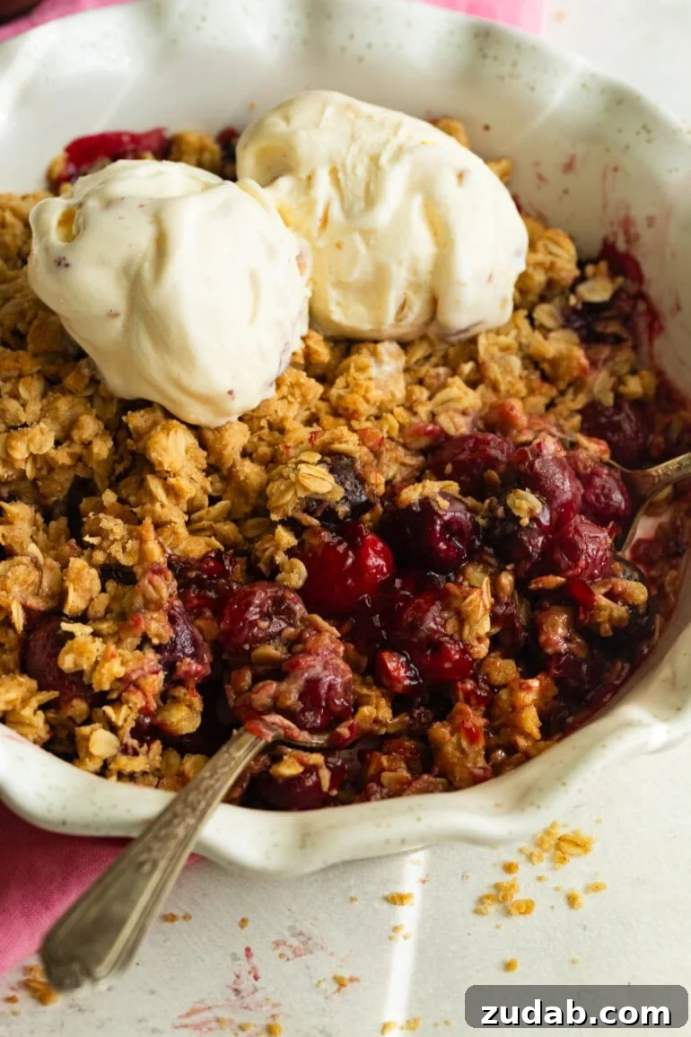 Classic Old-Fashioned Cherry Crisp with Oat Topping 6 someone scooping up a bite of cherry crisp topped with scoops of vanilla ice cream