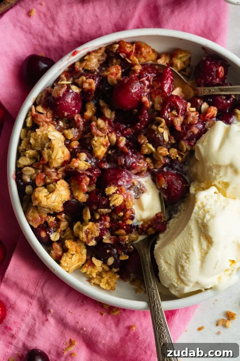 Classic Old-Fashioned Cherry Crisp with Oat Topping 8 a serving of cherry crisp in a small bowl melting vanilla ice cream on the side of the dish